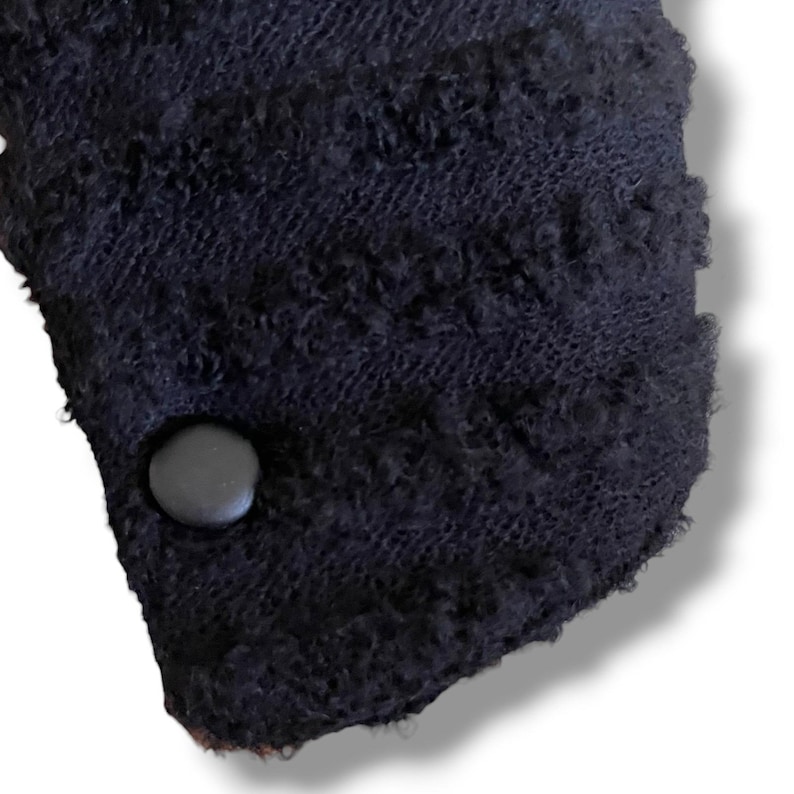 May include: Close-up of a section of a dark navy blue knitted fabric with a textured, looped pattern. A dark gray button is attached to the fabric. The fabric has a soft, fuzzy appearance.