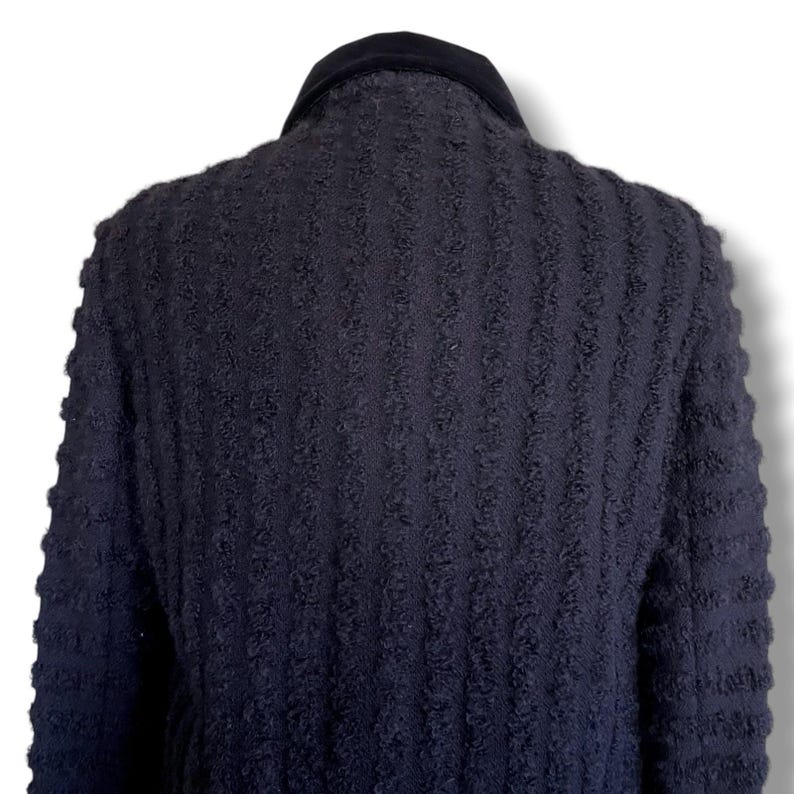 May include: A dark navy blue textured jacket with a black velvet collar. The jacket has a vertical ribbed pattern and is viewed from the back, showcasing the design and fabric texture. The garment appears to be a coat or blazer.