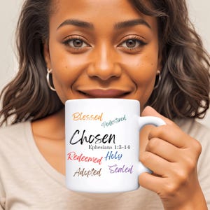 Puede incluir: Taza de cerámica blanca con las palabras "Blessed, Predestined, Chosen, Ephesians 1:3-14, Redeemed, Holy, Adopted, Sealed" en letras de colores.