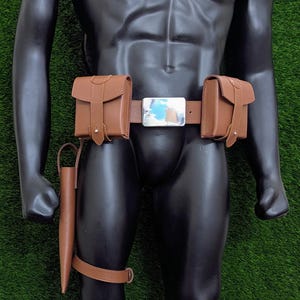 Puede incluir: Un cintur&oacute;n de cuero marr&oacute;n con dos bolsas a cada lado y una hebilla plateada. El cintur&oacute;n se lleva en un maniqu&iacute; con correas de pierna de cuero marr&oacute;n y bolsas.