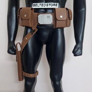 May include: Brown leather utility belt with multiple pouches and a holster, displayed on a mannequin. The belt features a silver-colored buckle and is complemented by a leg strap. The text "BELTEDSTORE" is visible.