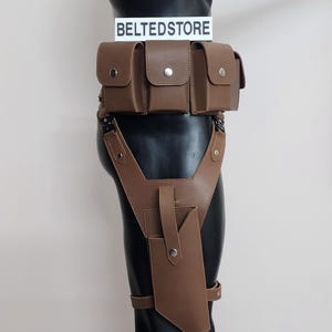 May include: Brown leather utility belt and thigh holster set. The belt features multiple pouches with snap closures. The thigh holster has a phone-sized pocket and adjustable straps. The text "BELTEDSTORE" is displayed on a white sign.