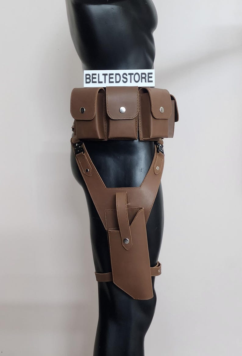 May include: Brown leather utility belt and thigh holster set. The belt features multiple pouches with snap closures. The thigh holster has a phone-sized pocket and adjustable straps. The text "BELTEDSTORE" is displayed on a white sign.