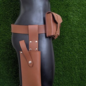 Puede incluir: Un cintur&oacute;n de cuero marr&oacute;n con una funda y una bolsa. La funda est&aacute; unida a la pierna izquierda y la bolsa est&aacute; unida a la cadera derecha.