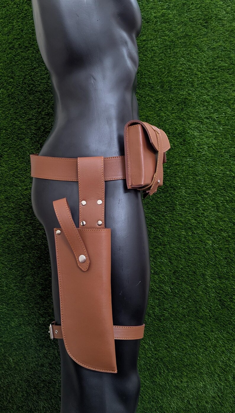 Puede incluir: Un cintur&oacute;n de cuero marr&oacute;n con una funda y una bolsa. La funda est&aacute; unida a la pierna izquierda y la bolsa est&aacute; unida a la cadera derecha.