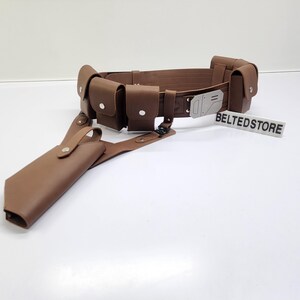 May include: A brown leather utility belt with multiple pouches and a holster. The belt has a silver buckle and is designed to be worn around the waist. The word "BELTEDSTORE" is printed on a white sign.