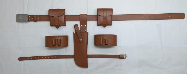 Puede incluir: Un cintur&oacute;n de cuero marr&oacute;n con dos bolsas de cuero marr&oacute;n, una funda de cuero marr&oacute;n y dos brazaletes de cuero marr&oacute;n. El cintur&oacute;n tiene una hebilla plateada y las bolsas tienen broches plateados.