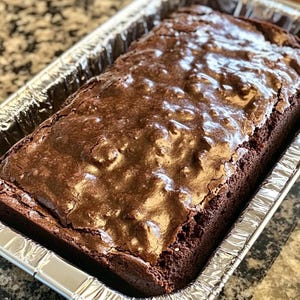 Op de afbeelding: Een grote rechthoekige pan met brownies met een glanzende chocolade glazuur. De brownies zitten in een zilveren folie pan.