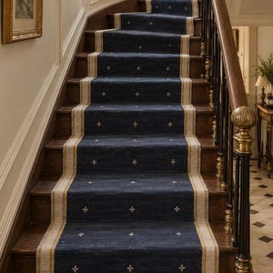 May include: A long, dark blue stair runner carpet featuring a repeating pattern of small, white, four-pointed star motifs. The runner has wide, light beige borders with thin, vertical gold-toned stripes running along both edges of the fabric.