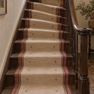 May include: A beige stair runner with a textured weave, featuring dark red and brown striped borders along both sides and small, repeating diamond-shaped patterns in a dark red hue centered across the length of the runner on wooden stairs.