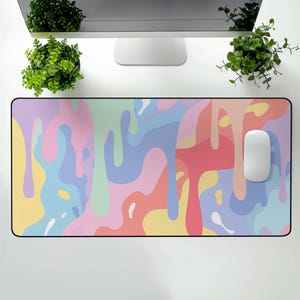 Puede incluir: Alfombrilla de ratón rectangular con un diseño abstracto colorido. La alfombrilla presenta un patrón de formas fluidas en colores pastel, incluyendo rosa, azul, amarillo y verde. Un ratón de ordenador blanco descansa sobre la alfombrilla.