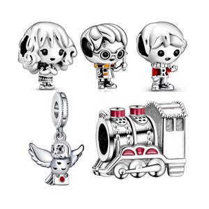 Könnte beinhalten: Eine Sammlung von silbernen Charms mit Charakteren und Elementen aus einer Fantasy-Serie. Die Charms umfassen einen Zug, eine Eule und drei Figuren. Die Charms sind mit schwarzen und roten Akzenten versehen.