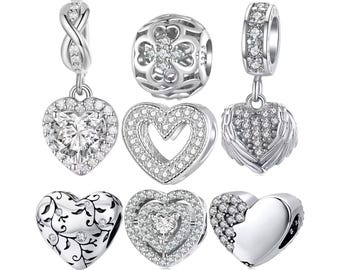 May include: A collection of silver-toned charm beads. The charms feature heart, clover, and infinity designs, embellished with clear crystals. Some charms have dangling heart pendants, while others are round or cylindrical.