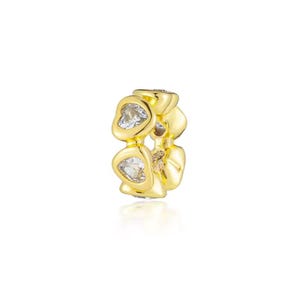 May include: A gold-colored charm with a series of heart-shaped cutouts, each holding a clear, sparkling stone. The charm is designed to be worn on a bracelet or necklace, adding a touch of elegance.