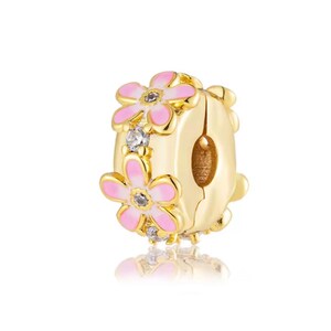 May include: A gold-toned charm bead featuring a central band decorated with pink enamel flower petals and small clear stones. The cylindrical bead has a polished metallic finish and a hollow center, designed to slide onto a bracelet or necklace chain.
