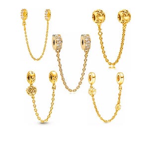 Può includere: Catene di sicurezza per ciondoli color oro con vari elementi decorativi. I ciondoli includono un motivo a raggiera, floreale, un cuore e un albero della vita. Ogni catena ha una chiusura su ciascuna estremità per attaccarsi a un braccialetto.