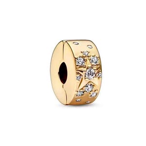 May include: Gold-colored charm with a star and crystal design. The charm features a central star motif surrounded by smaller crystals. The charm has a clasp design and is likely made of metal.