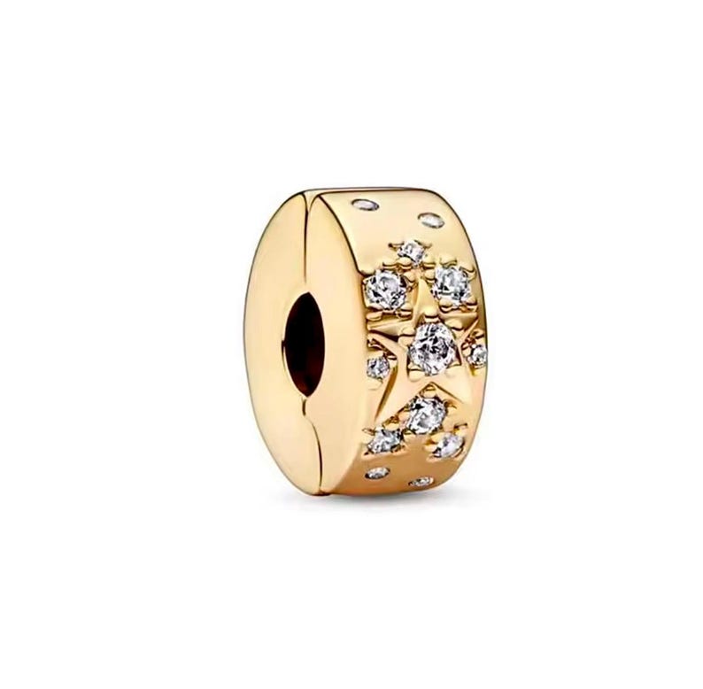 May include: Gold-colored charm with a star and crystal design. The charm features a central star motif surrounded by smaller crystals. The charm has a clasp design and is likely made of metal.