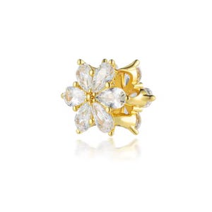 May include: A gold-colored floral-shaped charm with clear, teardrop-shaped gemstones. The charm has a detailed design with multiple petals and a central setting, creating a sparkling, elegant appearance. The charm is likely for jewelry.