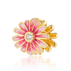 May include: A gold-toned metal charm shaped like a flower with layered petals featuring a gradient of pink and white enamel. The center of the flower is decorated with a small, clear, round faceted stone surrounded by a textured gold-toned border.