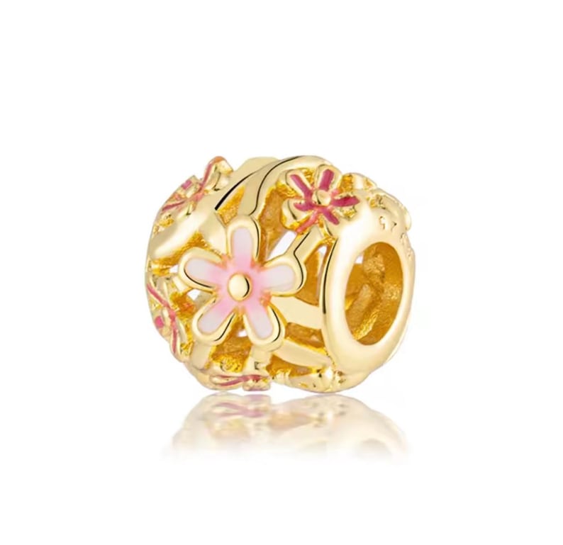 May include: A gold-toned charm bead featuring an openwork design with multiple five-petaled flowers. The flowers are accented with light pink and dark pink enamel detailing. The bead has a central hole for threading onto a bracelet or necklace chain.