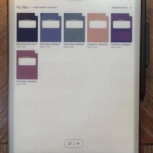 May include: A rectangular digital tablet displaying a file directory with notebook covers in various colors: black, blue, green, orange, purple, and red. The tablet has the word "reMarkable" at the top and a stylus attached to the side.
