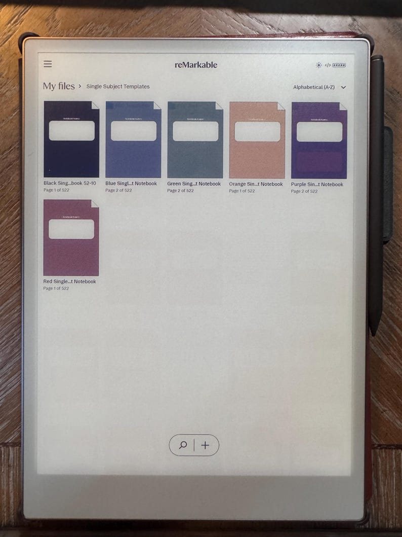 May include: A rectangular digital tablet displaying a file directory with notebook covers in various colors: black, blue, green, orange, purple, and red. The tablet has the word "reMarkable" at the top and a stylus attached to the side.