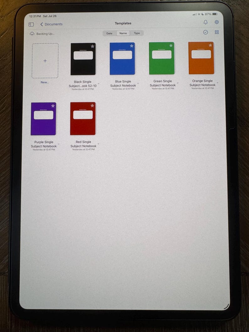 May include: A tablet screen displays a document with notebook templates. The templates include black, blue, green, orange, purple, and red notebooks. Each notebook has a white rectangle and a star icon. The screen also shows the time and date.