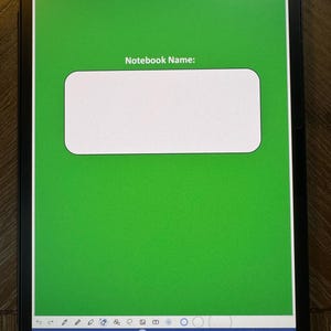 May include: A digital tablet displays a green notebook cover with the text "Notebook Name:" inside a white rectangular box. The tablet's screen shows the time and battery percentage. The bottom of the screen has a blue bar with various icons.