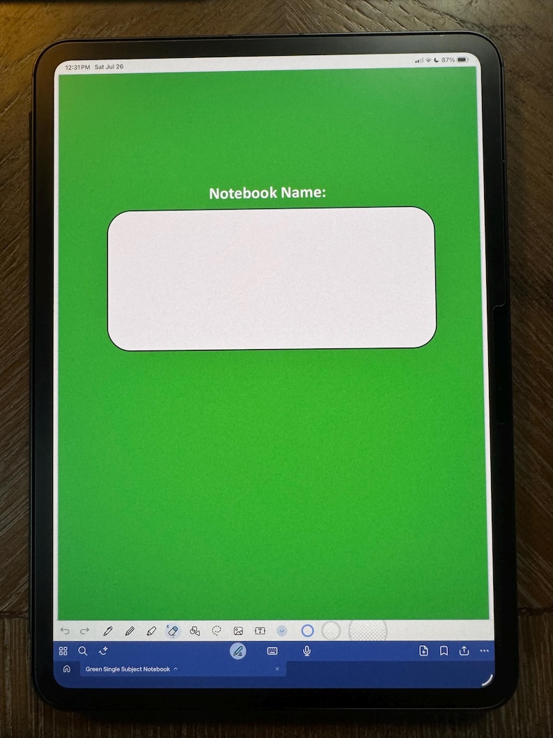 May include: A digital tablet displays a green notebook cover with the text "Notebook Name:" inside a white rectangular box. The tablet's screen shows the time and battery percentage. The bottom of the screen has a blue bar with various icons.