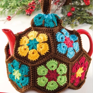 Może przedstawiać: Wełniany pokrowiec na czajnik z brązową podstawą i kolorowymi wzorami kwiatów w odcieniach żółtego, czerwonego, niebieskiego, zielonego i turkusowego.