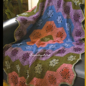 Puede incluir: Una colorida manta de ganchillo hecha a mano con un diseño floral. La manta presenta un diseño hexagonal con tonos de rosa, naranja, azul, verde y morado. La manta está sobre una superficie oscura.