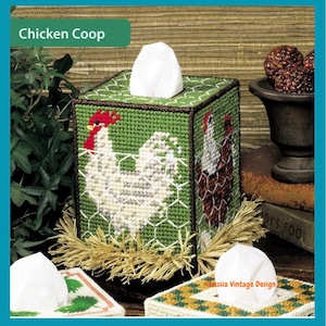 May include: A green, hand-stitched tissue box cover with a chicken coop design. The box features a white rooster with a red comb and a brown and white hen. The text "Chicken Coop" is displayed on the top left.