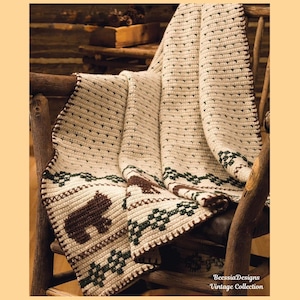 May include: Cream-colored crocheted blanket with a brown bear and tree design. The blanket is draped over a wooden chair. The border is a dark brown color. The blanket has a textured pattern and is part of the BeessiaDesigns Vintage Collection.