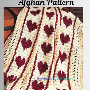 May include: Cream-coloured crochet afghan with a heart pattern. The afghan features rows of burgundy hearts and burgundy borders. The text "Crochet Heart Afghan Pattern" is at the top of the image, and the text "Bessiasvintagecollection" is at the bottom.