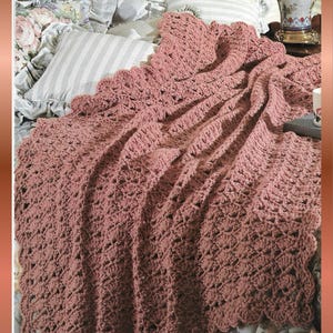 May include: A dusky pink crochet blanket with a scalloped edge, draped over a bed with floral and striped pillows. The blanket's texture is visible, and the overall aesthetic is vintage. The text "Beessia Vintage Design" is in the bottom right corner.