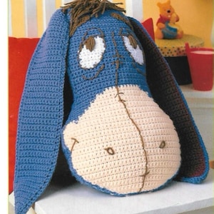 May include: A handmade crochet Eeyore plush toy. The plush features a blue head and ears, a cream-colored belly, and brown accents for the eyes, mouth, and mane. The toy is designed to resemble the character from Winnie the Pooh.