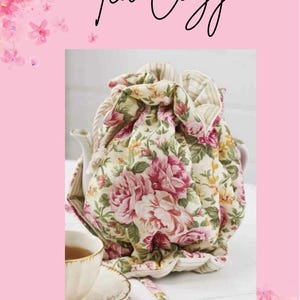 May include: A floral tea cosy with a cream background and pink and red roses. The tea cosy is covering a white teapot. The image has the words "Tea Cozy" in cursive script.