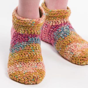 Può includere: Un paio di stivaletti pantofola all'uncinetto fatti a mano e colorati. Gli stivali presentano un mix di filato rosa, giallo, blu e arancione. I polsini alla caviglia sono ripiegati. Il filato ha una consistenza maculata. Le pantofole sono progettate per tenere i piedi al caldo.