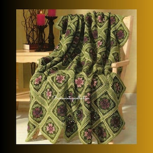 Può includere: Una coperta all'uncinetto verde fatta a mano con un motivo floreale drappeggiata su una sedia di legno. La coperta presenta motivi quadrati con disegni floreali rosa e viola scuro. Un elemento d'arredo per la casa.