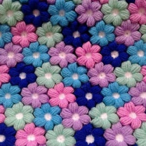May include: A close-up of a crocheted blanket with a repeating pattern of flowers in shades of blue, pink, green, and purple.