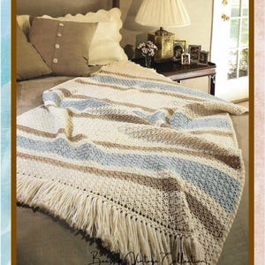 May include: A handmade crochet blanket with cream, light blue, and brown stripes, and a cream fringe. The blanket is draped over a bed with pillows and a nightstand. The text "Beessm Vintage Collection" is visible.