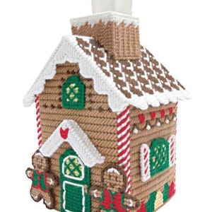 Puede incluir: Una funda de caja de pañuelos hecha a mano con forma de casa de jengibre. La casa marrón presenta adornos blancos, una chimenea y una puerta y ventanas verdes. Dos hombres de jengibre decoran el frente. Acentos a rayas rojas y blancas.