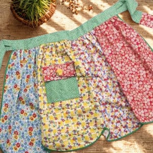 May include: A vintage apron with a patchwork design. The apron features floral patterns in blue, yellow, and red, with a green polka dot trim and ties. A green pocket is sewn onto the apron. The apron is made of fabric.