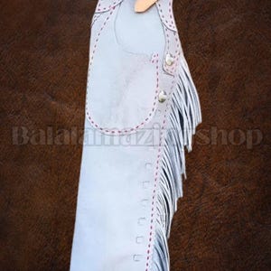 Puede incluir: Chaps de cuero gris claro con costuras decorativas y flecos. Los chaps tienen un cinturón de cuero con hebilla. El texto "Balatamazishop" es visible en la parte inferior izquierda.