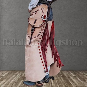 May include: Beige leather chaps with red fringe and decorative stitching. The chaps feature a pocket, a buckle, and a metal ring. The chaps are worn with blue jeans and cowboy boots. The text "Balala Wing Shop" is visible.