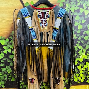May include: A brown leather jacket with fringe and beading. The jacket has a blue and white pattern on the sleeves and a red, white and brown pattern on the back. The jacket is hanging on a black hanger. The text "BALALA AMAZING SHOP" is visible on the jacket.