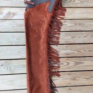 May include: Brown leather chaps with fringe and a decorative design on the top.