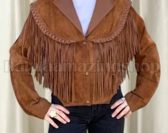 May include: A brown suede jacket with long sleeves and a collar. The jacket features a fringe design across the chest and shoulders. The jacket has a button-up front and is worn with black jeans.