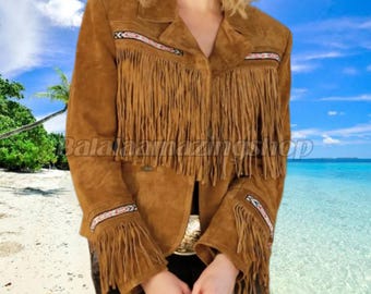 May include: A brown suede jacket with fringe detailing on the chest and sleeves. The jacket has a collared neckline and decorative beading along the fringe. The jacket is a neutral color and has a classic Western style.